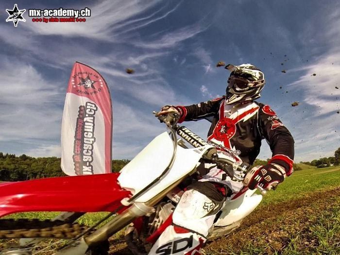 Motocross-Fahrer in der Kurve, im Hintergrund die MX-Academy-Fahne