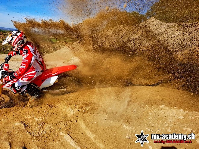 Motocross rider in a sandy turn with sand spraying up